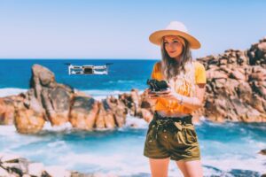 Mujer volando un dron entre las rocas de una playa